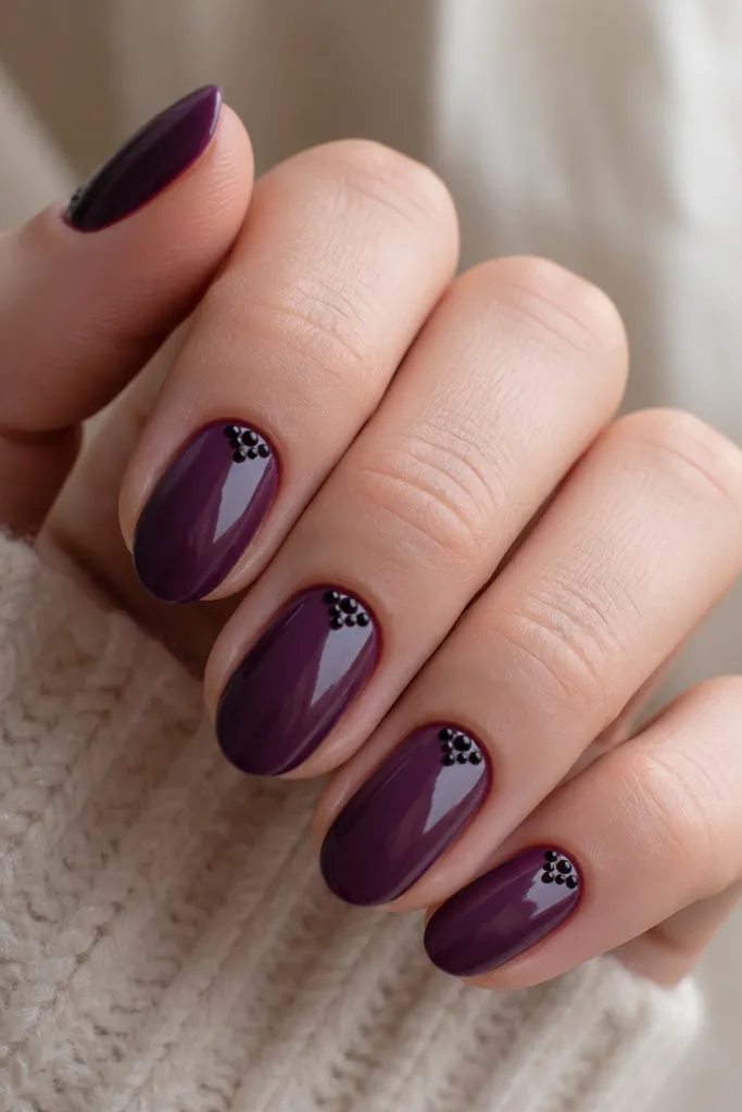 Dark purple nails with a small cluster of black dots at the cuticle on each nail; the rest of the nail stays clean and glossy.