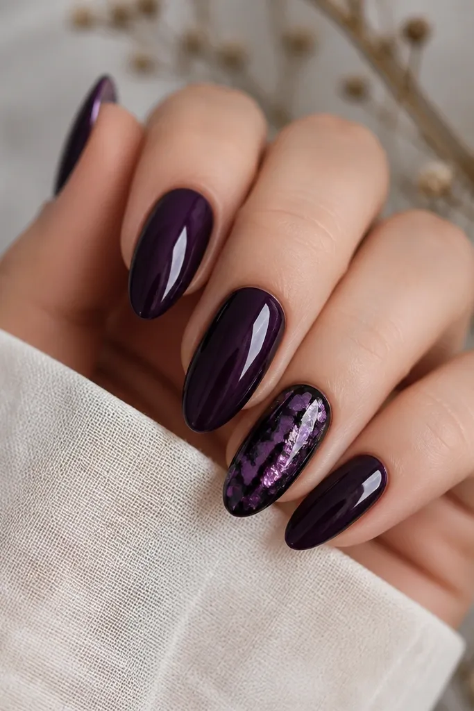Four nails in deep dark purple; one accent nail has black and purple foil flakes scattered irregularly, glossy and reflective like broken glass.