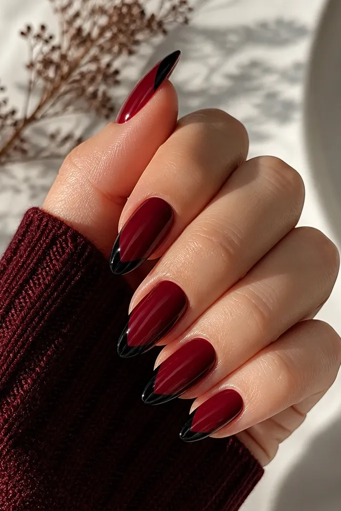 Glossy burgundy almond nails with a crisp black V-shaped notch at the tip, like a backward chevron; clean edges, high shine.