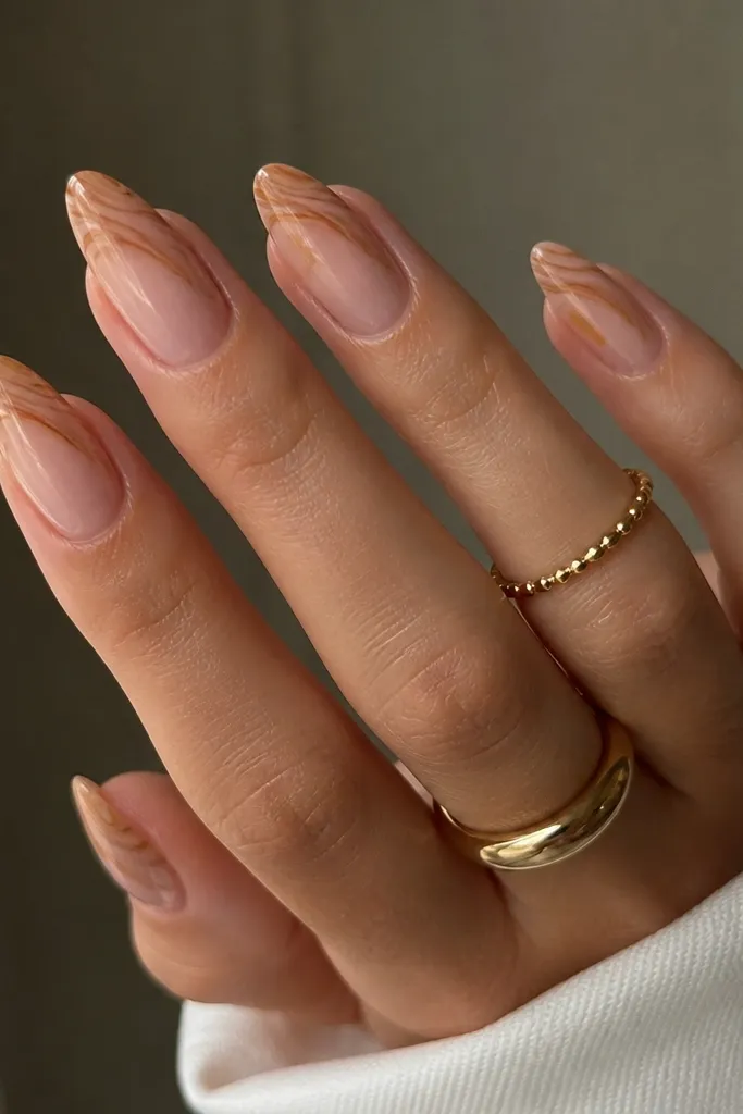 Nude almond nails with caramel swirl lines concentrated at the tip, like a soft ribbon; glossy finish; negative space visible.
