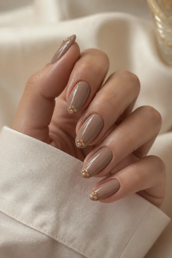 Mocha nude almond nails with a single small 3D beaded cluster at the tip center; beads look like tiny pearls in caramel and gold; glossy top coat.