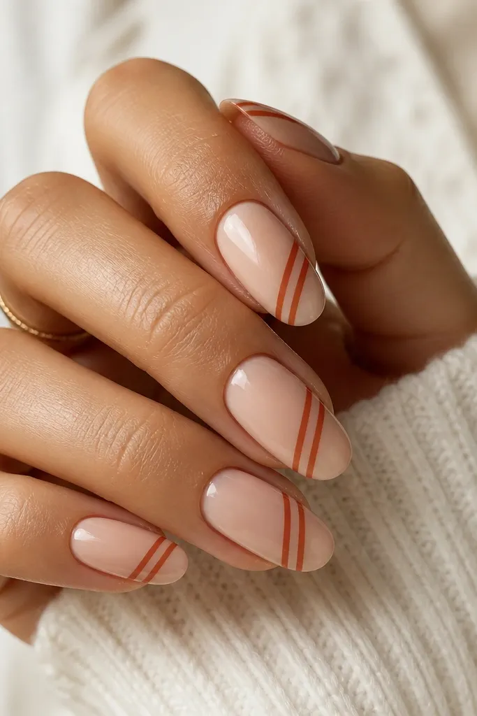 Medium oval nails in a nude base; two thin rust-orange diagonal stripes sit on each nail, angled from lower left to upper right. The stripes are crisp and glossy.