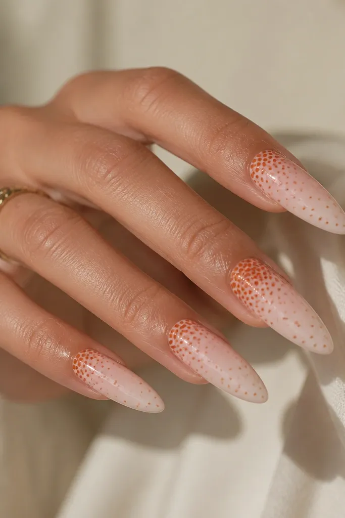 Long almond nails in nude pink; dots in burnt orange fade from dense at the cuticle side to sparse toward the tip. The ring finger has the densest cluster.