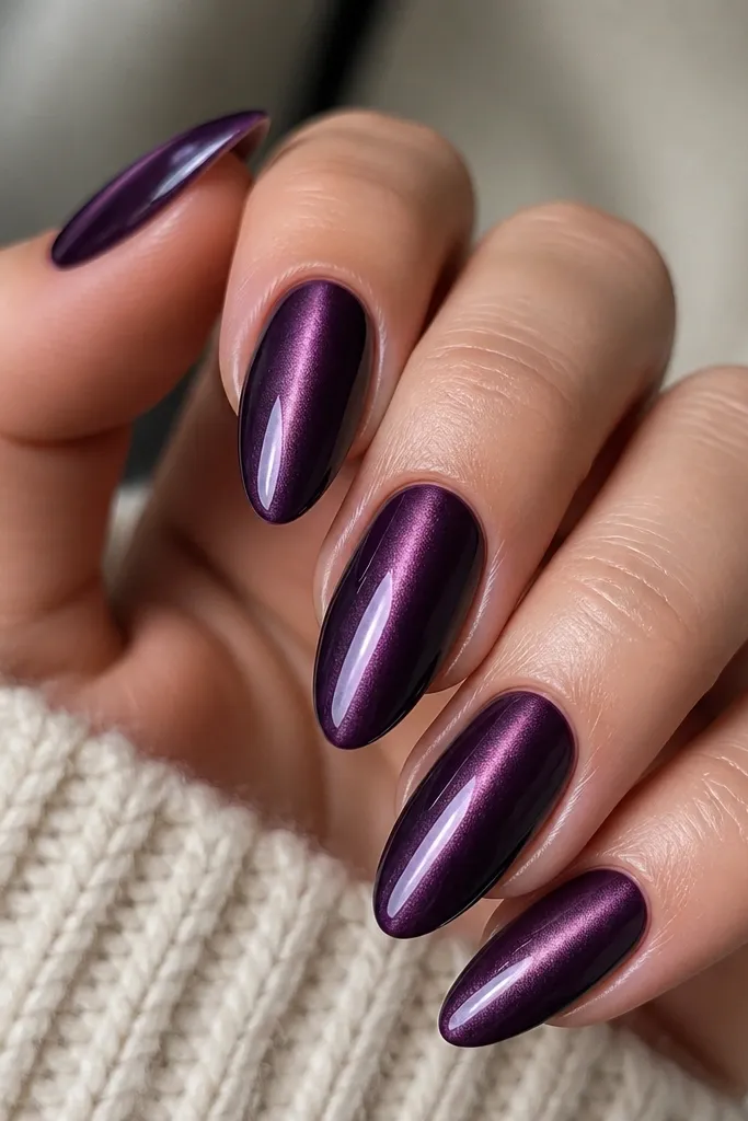 A set of medium almond nails painted a deep eggplant purple. Each nail has a single bright cat-eye stripe running down the middle, with a soft velvet glow that fades near the edges. The top coat is mirror-gloss and the cuticles look sharply cleaned.