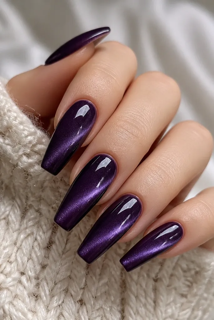 Long coffin nails in deep midnight grape purple. The cat-eye stripe angles diagonally from near the cuticle toward the outer edge, creating a slanted "eye" glow. The finish is glossy with no matte patches.