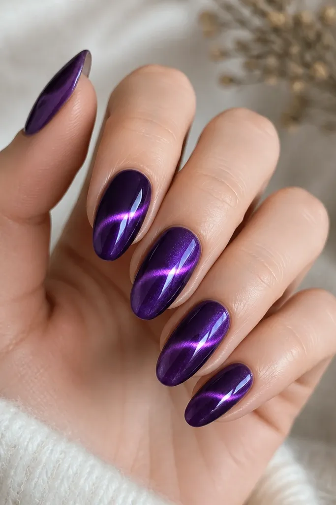 Medium almond nails in royal purple. The cat-eye line is bright and slightly thicker in the center, with a subtle second glow that appears just above it. The nails have a smooth, high-gloss finish.