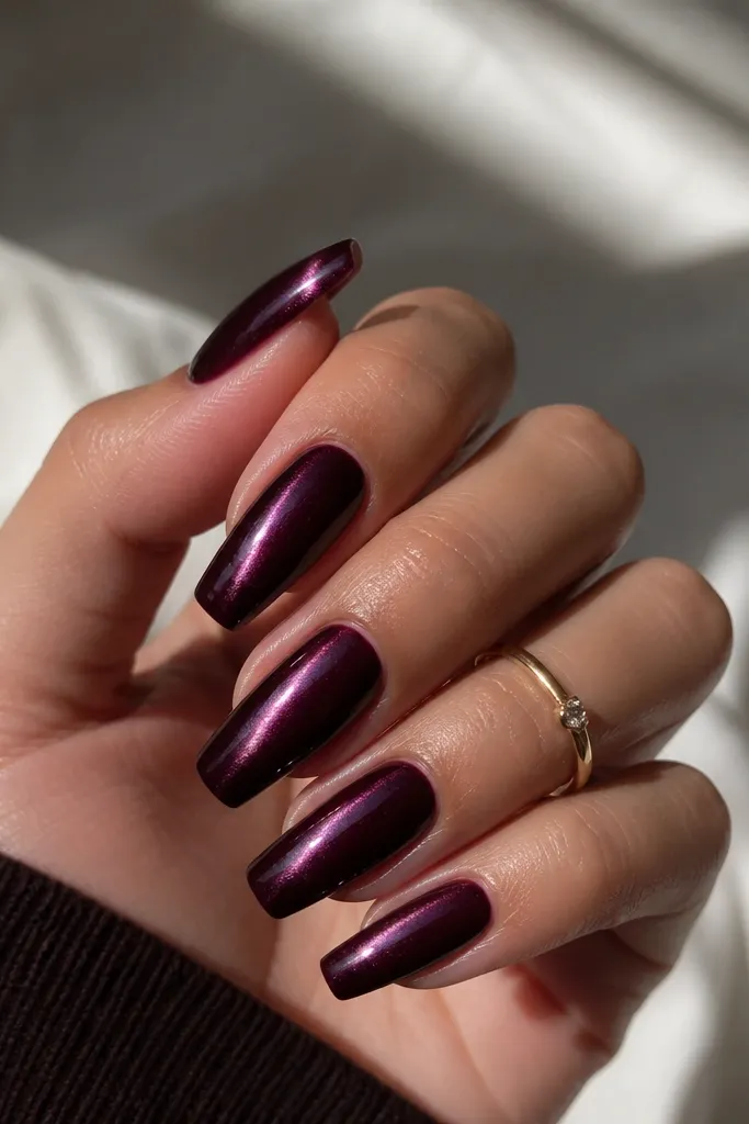 Coffin nails painted near-black cherry purple. The cat-eye stripe starts bright at the cuticle and fades to a softer glow near the tip. The finish is glossy and smooth.