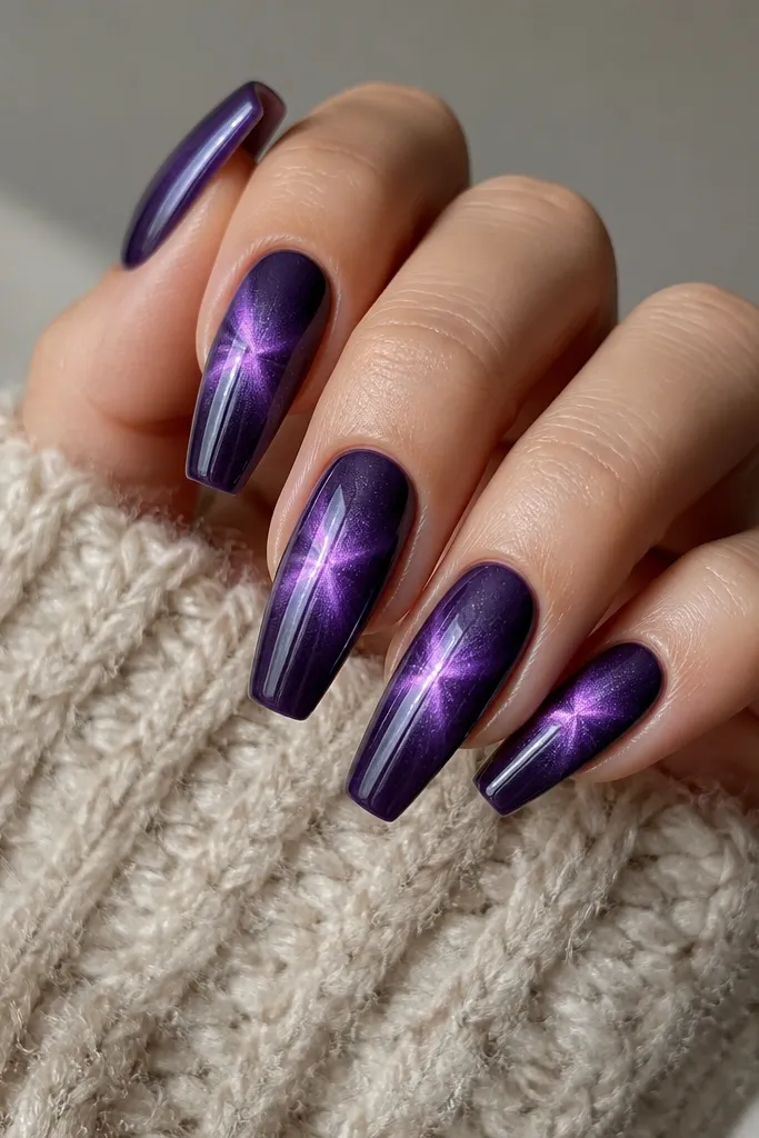 Coffin nails in dark purple with a cat-eye stripe that fans out slightly at the center, like a starburst around the eye. The stripe is still readable, but there's extra glow around it. Glossy finish and smooth edges.