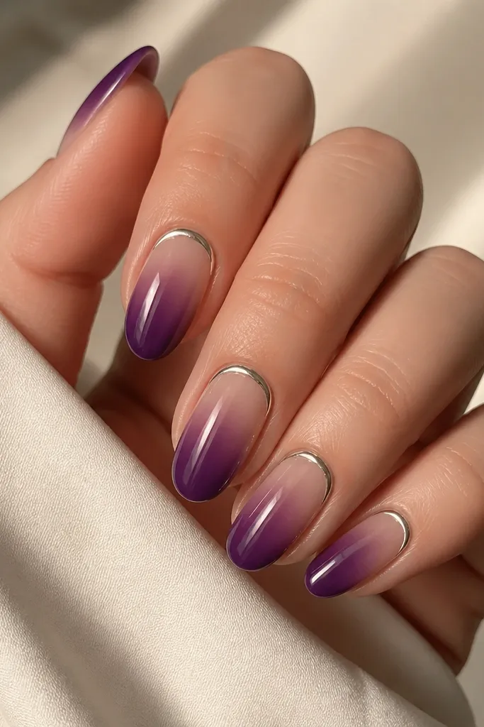 A set of medium oval nails in a grape jelly gradient. The base is sheer at the cuticle fading into a darker purple toward the tip. Silver half-moons sit right at the cuticle line, thin and reflective, with a glossy top coat.