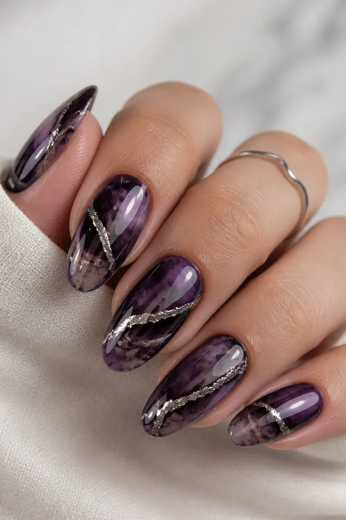 Oval nails with dark purple marble swirls, glossy and dimensional. A bright silver vein runs diagonally across each nail, like a crack filled with metal, fading near the tip.