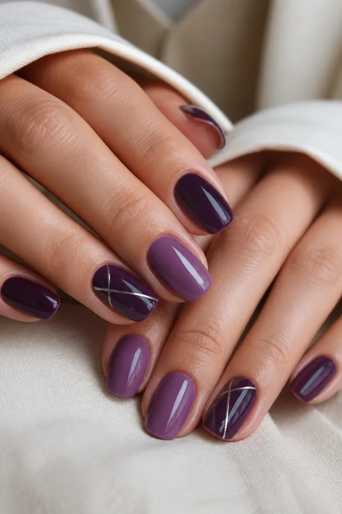 A mixed set: some nails are deep plum, others are lighter grape plum, and two nails have dark purple base with thin silver lines. The silver lines are straight and glossy, with a consistent shine across the set.