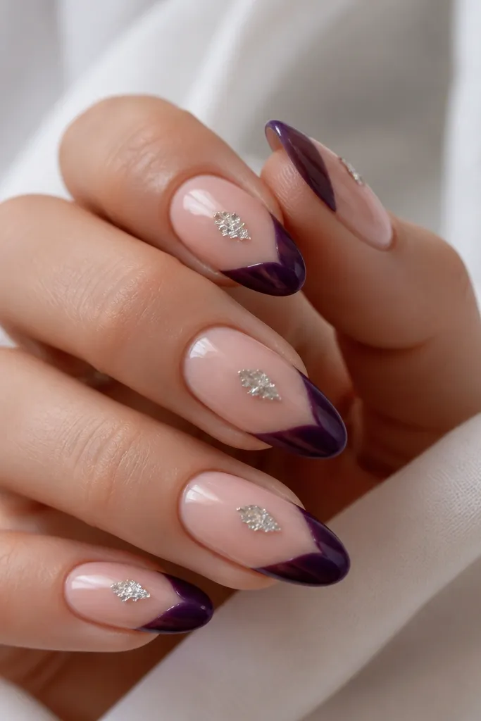 Almond nails with a dark purple French tip that is curved and swirly, not straight. In the center of the nail, there's a silver "knot" made of a small cluster of foil pieces. Glossy and clean.