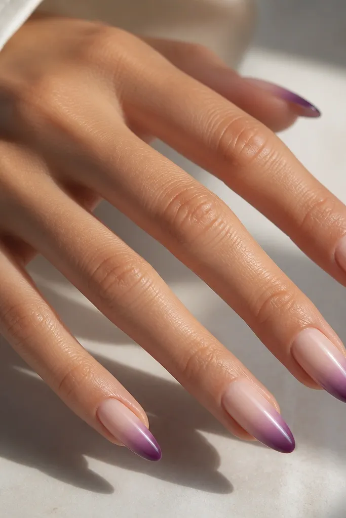Long almond nails with a milky nude base; French tips fade from dark grape at the tip to a lighter purple toward the center; glossy finish.