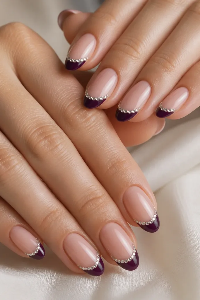 Medium oval nails with nude base; dark purple French tips; a single row of tiny clear rhinestones following the smile line; glossy top.