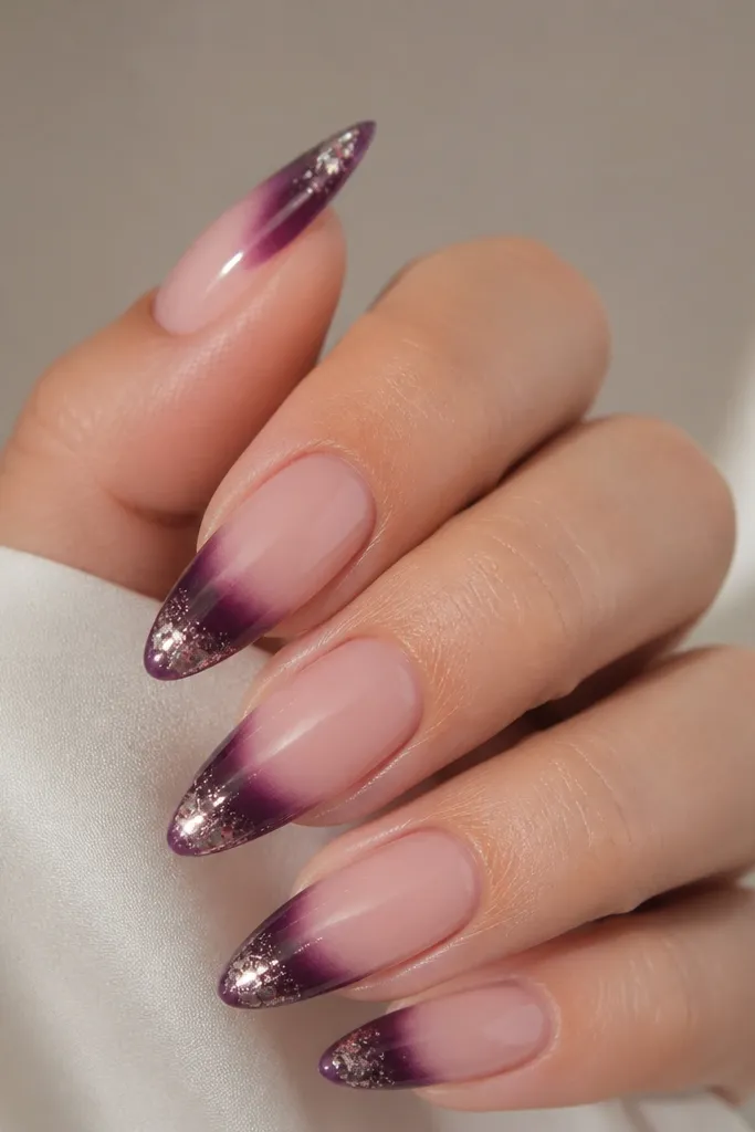 Almond nails with nude base; dark purple tips that fade into a metallic foil shimmer near the very edge; glossy top and reflective foil.