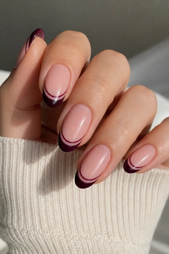 Medium oval nails with nude pink base; dark plum French tips with a thin second line inside the tip border; glossy finish.