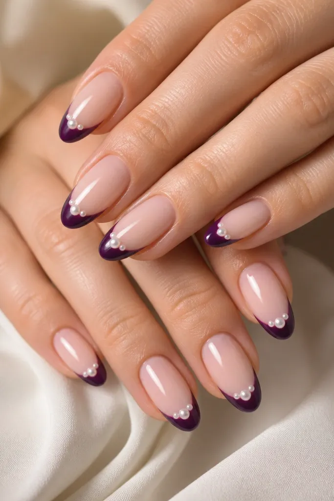 Almond nails with sheer nude base; dark purple French tips; a small cluster of three pearlized dots near the center of each tip; glossy finish.