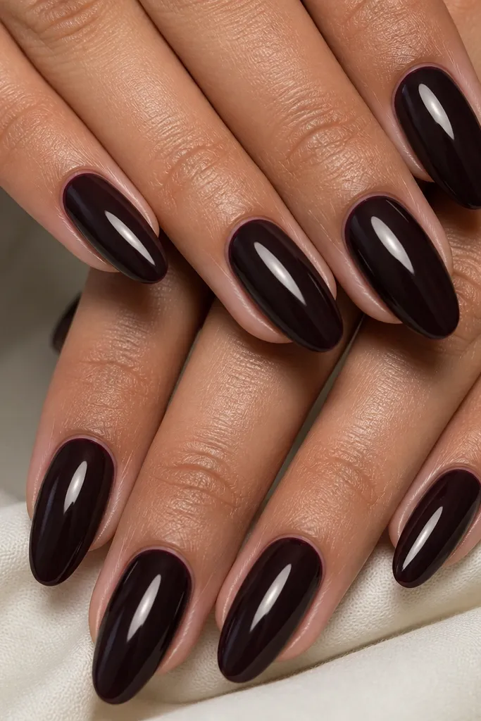 Ten almond nails painted a near-black espresso purple, glossy finish, with a smooth even cuticle line and a subtle light reflection streak down the center of each nail.