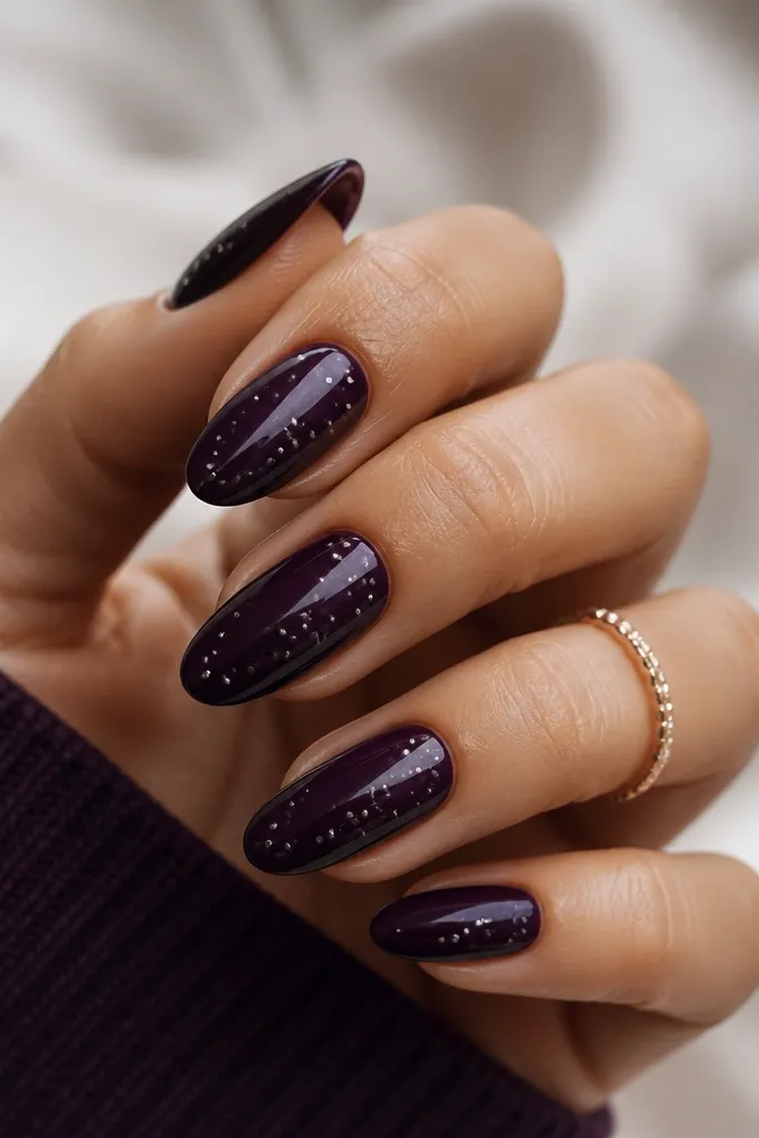 Dark purple almond nails with tiny silver micro dots scattered near the center and upper third, like a subtle constellation, with a glossy finish.