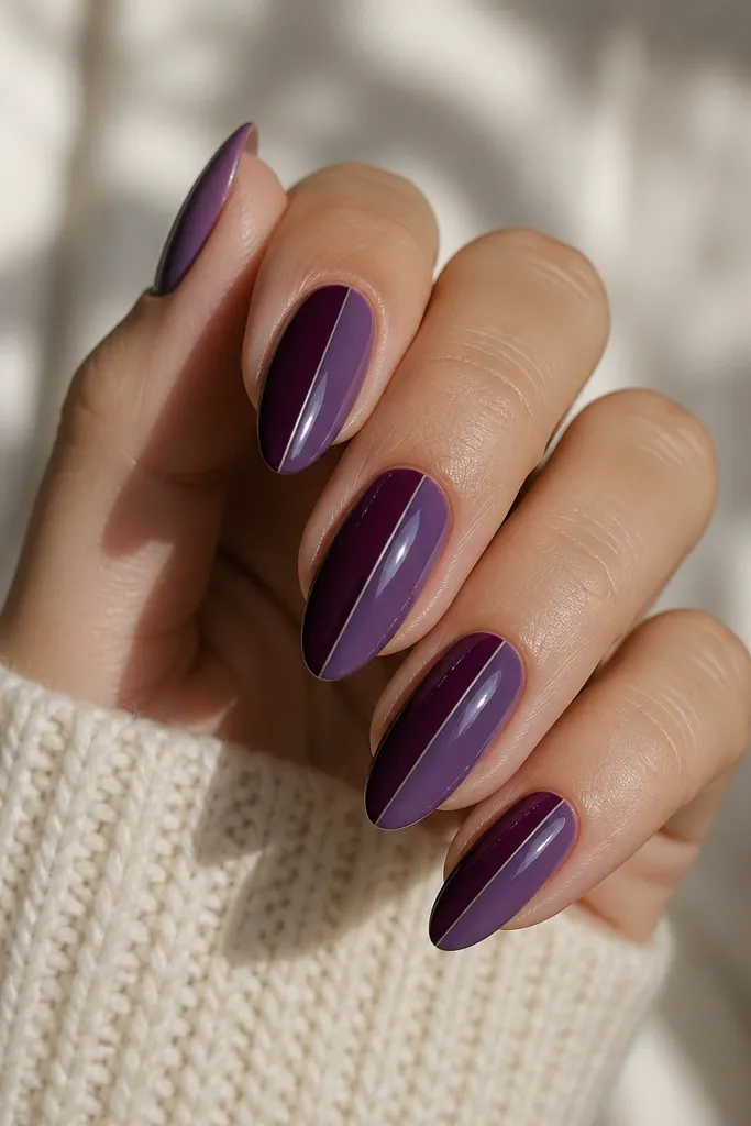 Almond nails split vertically into two shades of purple separated by a crisp thin line, one side deep plum and the other side slightly lighter violet, glossy finish.