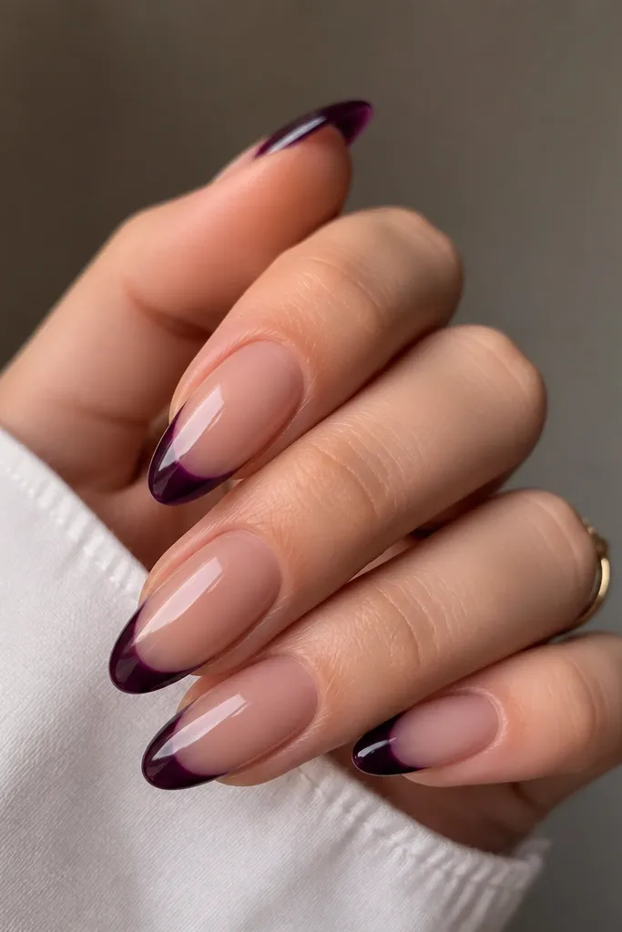 Almond nails with a sheer nude base and ultra-glossy dark purple tips that look like tinted glass, with a smooth curved edge and no harsh lines.