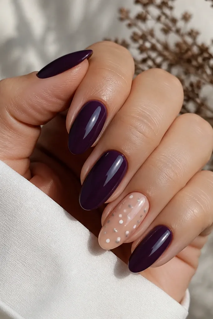 Most almond nails are solid dark purple glossy. The ring finger has a nude base with evenly spaced tiny white and silver polka dots, with crisp dot edges.