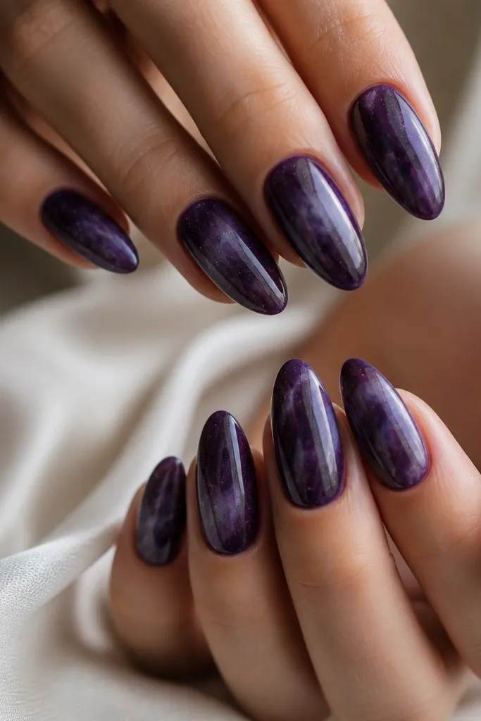 Glossy dark purple almond nails with soft smoky galaxy smudges and tiny scattered silver specks, giving a cloudy space look without sharp stars.