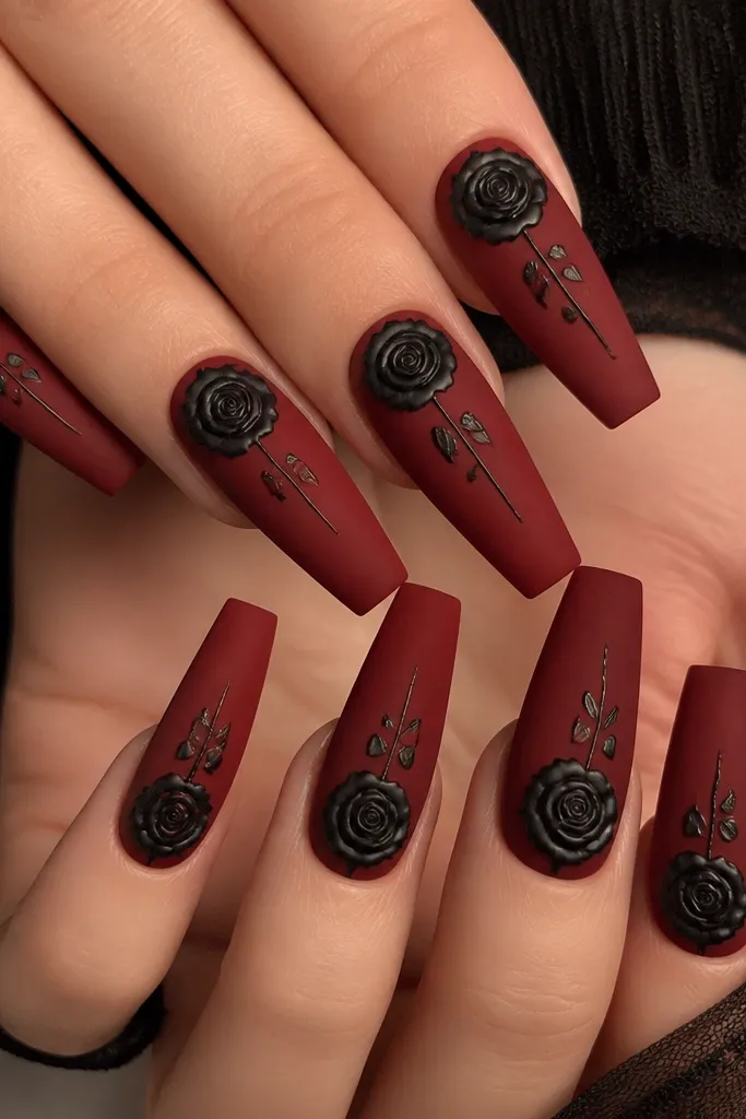 Long coffin nails. The base is matte deep red. On each nail, a black rose illustration sits near the cuticle and curves toward the center, with thin stem lines. The roses have a slightly raised look under topcoat.