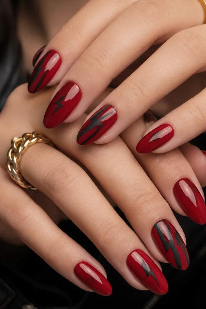 Medium almond nails. Base is glossy deep red. A few nails have black matte lightning bolt shapes angled diagonally from near the cuticle to the tip. Other nails are solid red with one tiny matte black bolt near the lower third.