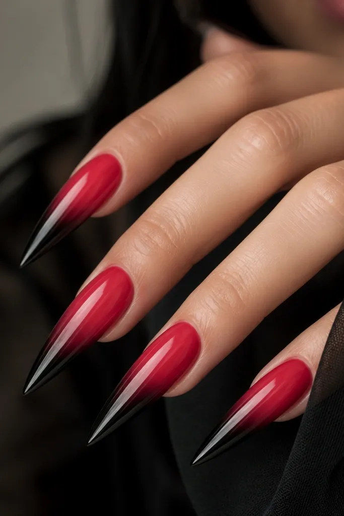 Long stiletto nails. The base is a smooth red gradient that fades lighter toward the center, then transitions into black at the tips like smoke. The edges are soft and blended, with a glossy finish overall.