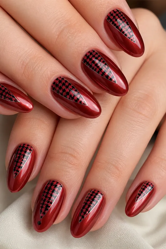 Short-to-medium almond nails in a glossy cherry-red chrome finish, with black houndstooth pattern panels starting at the cuticle and tapering toward the center of each nail. The pattern is sharp and high-contrast, outlined by a thin clear border so it looks like a graphic sticker under the topcoat. Accent nail has a slightly larger houndstooth patch and a tiny black dot near the free edge.
