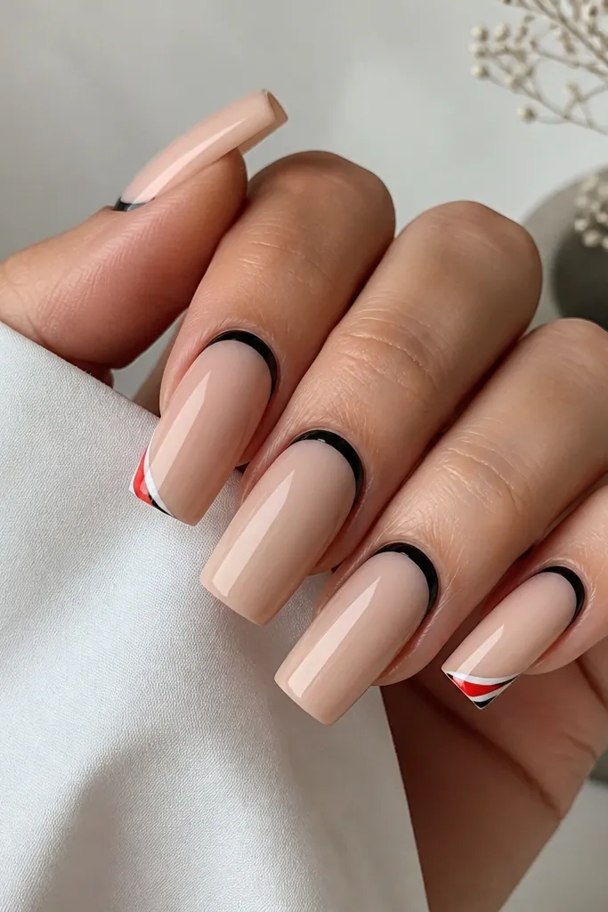Long square nails with a nude base. The reverse French is black, forming a curved line at the cuticle. On two nails, a small red-and-white corner design sits at the outer edge of the nail near the tip.