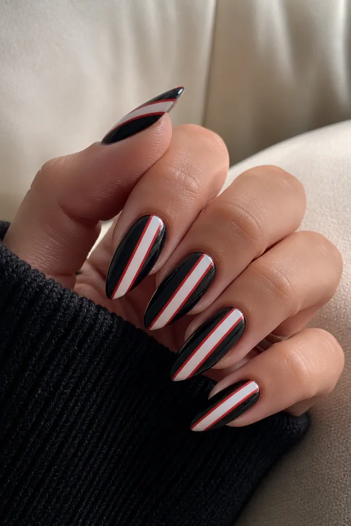 Medium almond nails painted glossy black. Two diagonal red stripes cross each nail. Between the stripes, a clean white negative-space band runs straight down the nail.