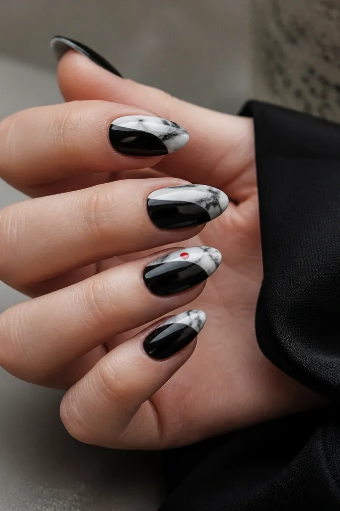 Medium almond nails with a glossy black base. The top third has white marble tips with swirling grayish-black lines. On one nail, a single red dot sits near the side of the marble tip.