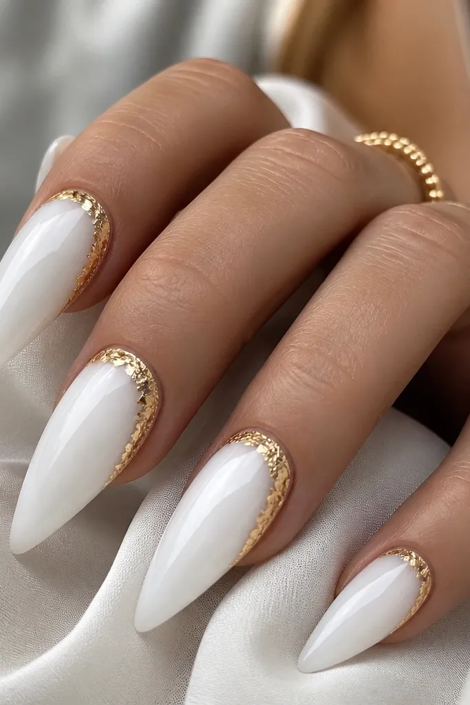 Long white stiletto nails with a glossy milky base. Each nail has a curved crescent of irregular gold foil starting near the cuticle and arcing toward the sidewall, leaving the rest of the nail plain white.
