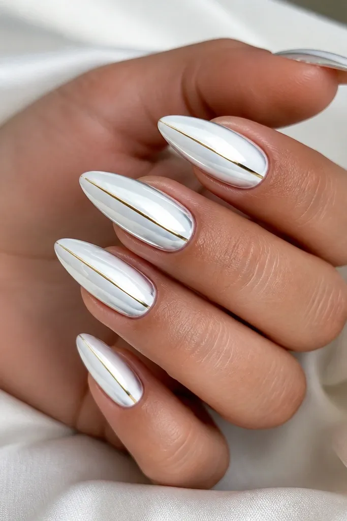 White chrome stiletto nails with a mirror finish. A single thin gold striping line runs vertically down the center on each nail, stopping about 1 millimeter above the tip.