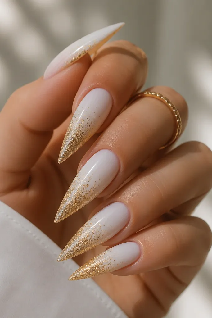 Stiletto nails with a glossy white base that fades into gold glitter toward the tip. The glitter is denser at the end and lighter near the middle.