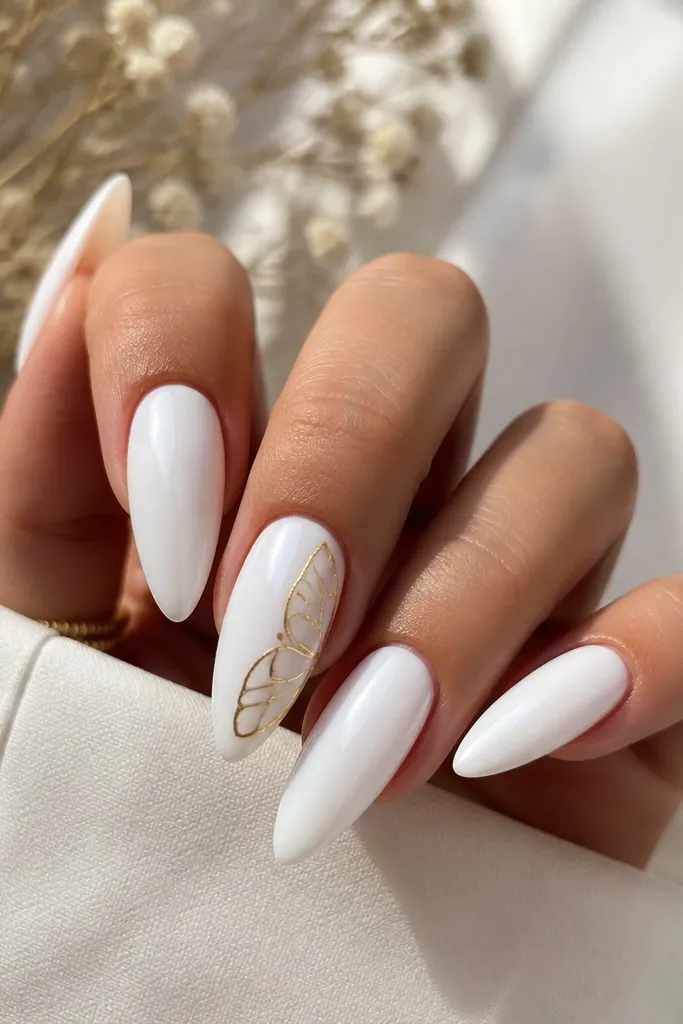 White glossy stiletto nails with a small gold butterfly wing decal or hand-painted wing near the side of the middle. The rest of the nail stays clean and glossy.