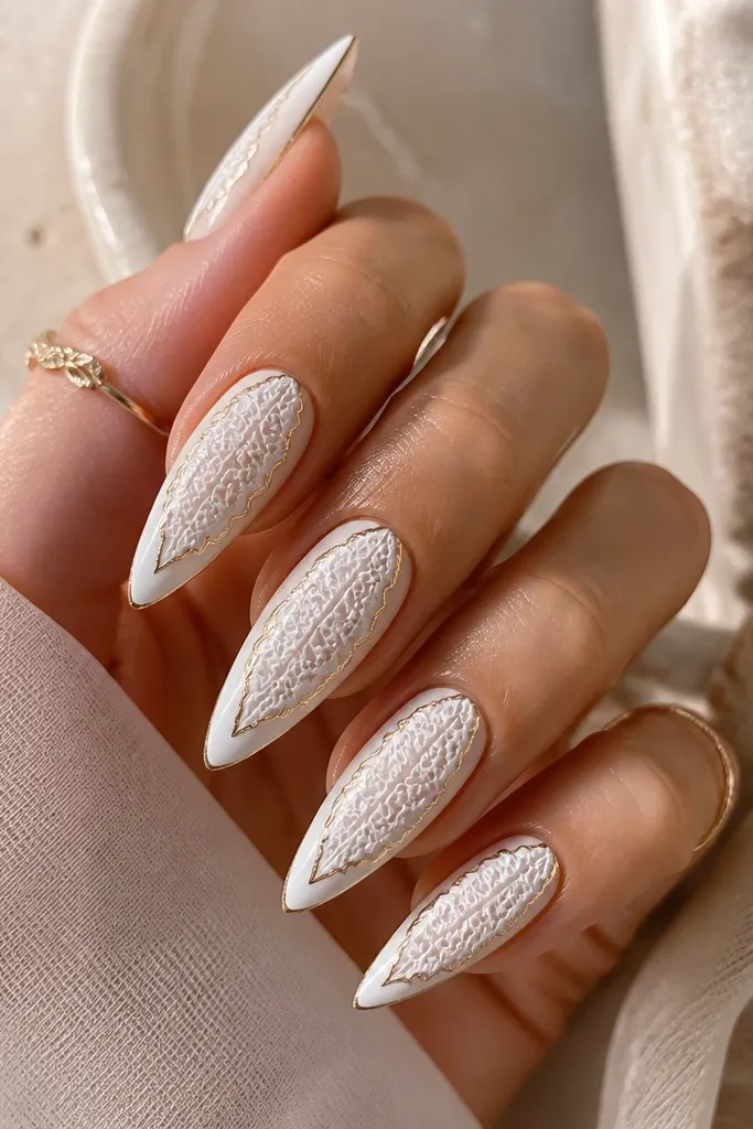 White stiletto nails with a lace-like pattern in raised white gel across the center. A thin gold outline runs around the lace shape like a frame.