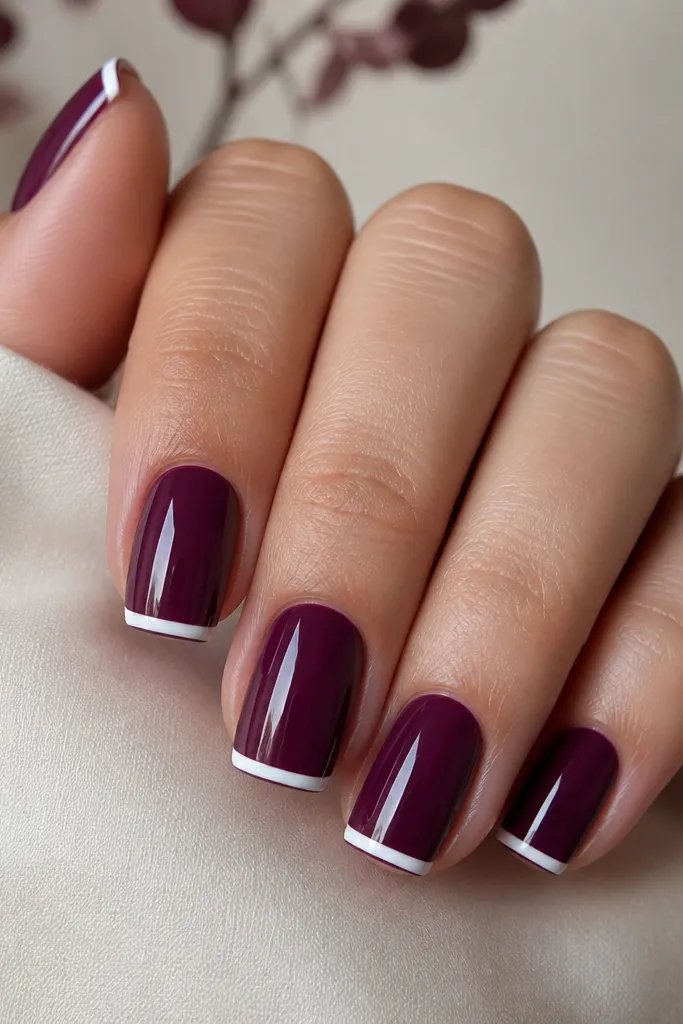 Medium square nails in a plum creme finish. Each nail has a very thin, straight white French line at the tip, about 1 millimeter thick. The rest of the nail is solid plum with a high-gloss top coat.