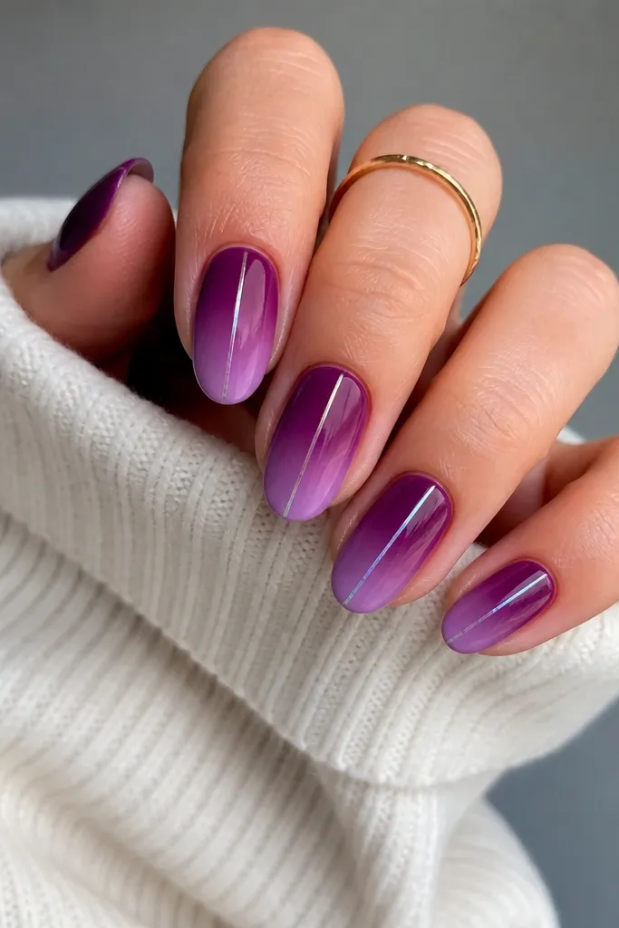 Medium oval nails with a vertical gradient: deeper plum near the cuticle fading into a lighter lilac-purple toward the tip. A single thin metallic lilac line runs straight down the center of each nail. Glossy finish.