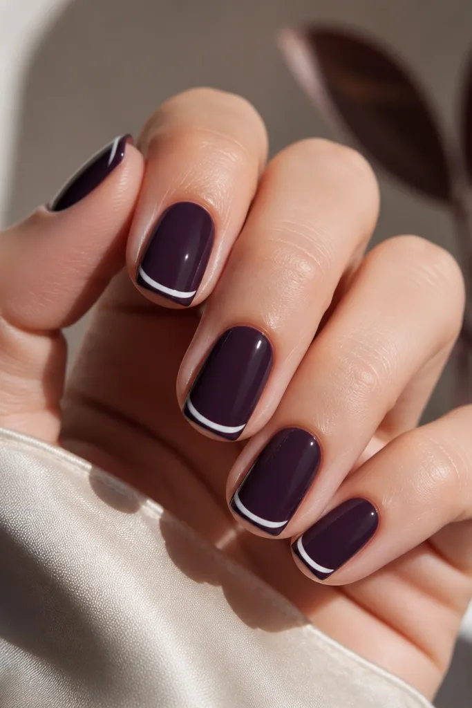Short squoval nails with a glossy dark purple base. The tips are dark purple too, but the design shows a thin white half-swirl at the tip edge on each nail, like a curved bracket. The rest stays solid.