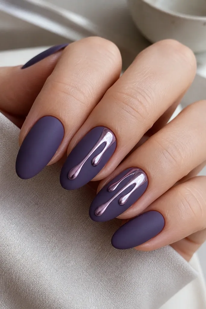 Medium almond nails in matte grape purple. On two nails, chrome powder forms teardrop streaks running from the middle toward the tip, like melted metal drips. Other nails are solid matte purple.