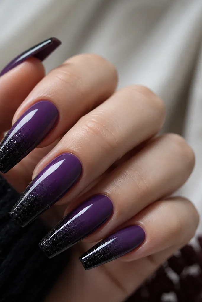 Long coffin nails with a soft ombre: deep purple at the cuticle fading into a darker almost-black at the tip. Over the ombre, a fine black micro-glitter is concentrated near the tip. Glossy top coat.