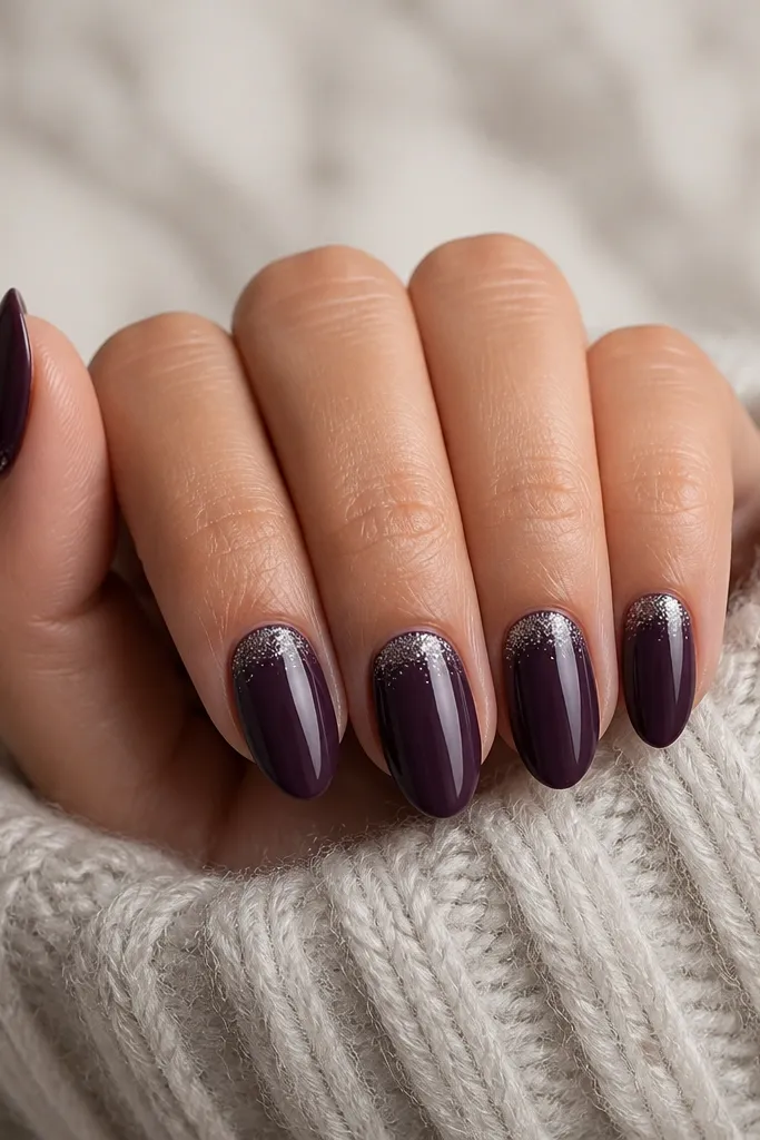 Short almond nails in glossy dark purple. A soft halo of tiny silver micro-glitter sits right under the cuticle on each nail, fading outward. No glitter exists on the rest of the nail.