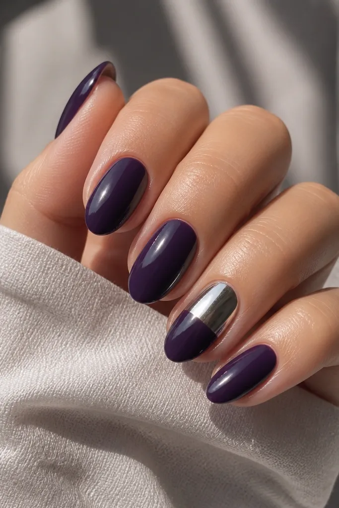 All nails are glossy dark purple. The ring finger has a half-chrome effect: the top half of the nail is mirror silver chrome, while the bottom half stays deep purple. Other nails are plain solid purple.