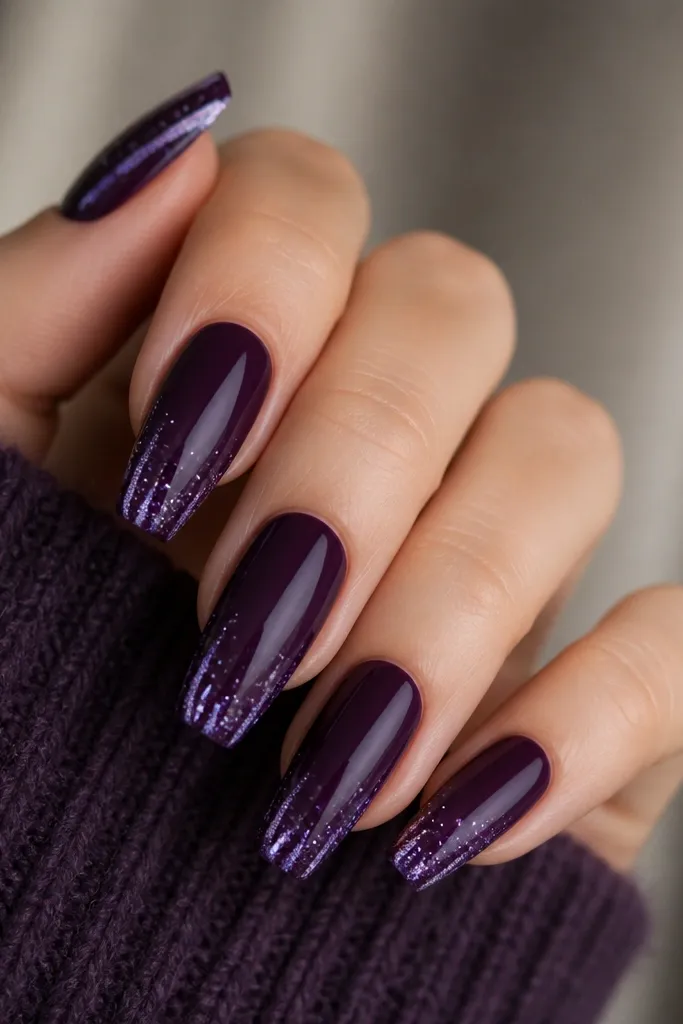 Medium coffin nails with glossy eggplant purple. At the very tip edge, a galaxy drip effect runs downward slightly: tiny white and lavender dots with a few glitter specks, like paint dripping. The rest of the nail is smooth solid purple.