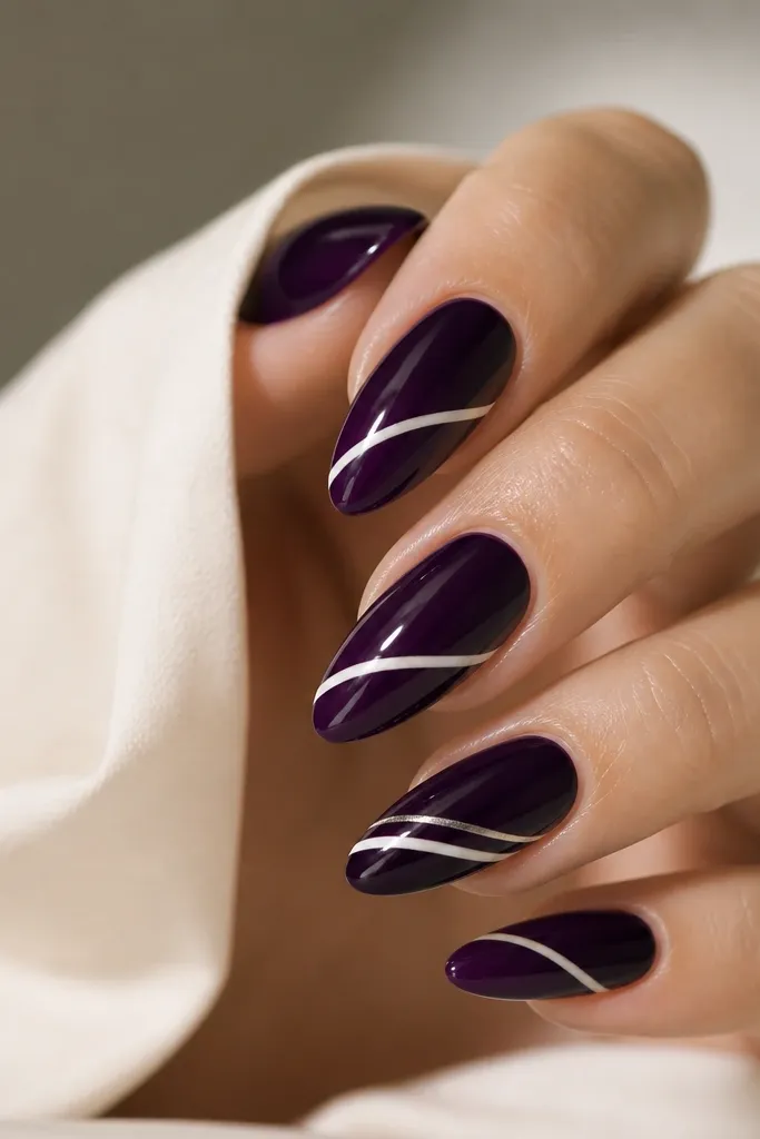 Long almond nails painted glossy dark purple. A diagonal white line wraps from the lower sidewall up toward the tip, crossing the nail center and continuing slightly onto the opposite side. Some nails have a second thin silver line parallel to it.