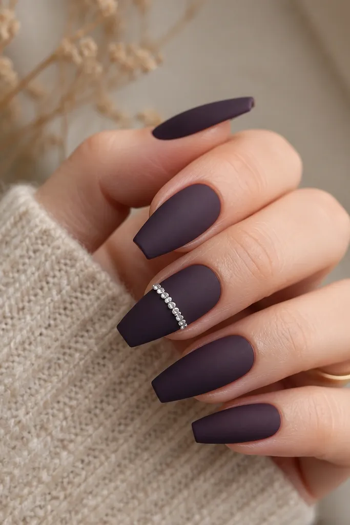 Medium coffin nails painted matte dark purple; one nail has a neat horizontal line of small clear rhinestones across the center, with the other nails plain matte.