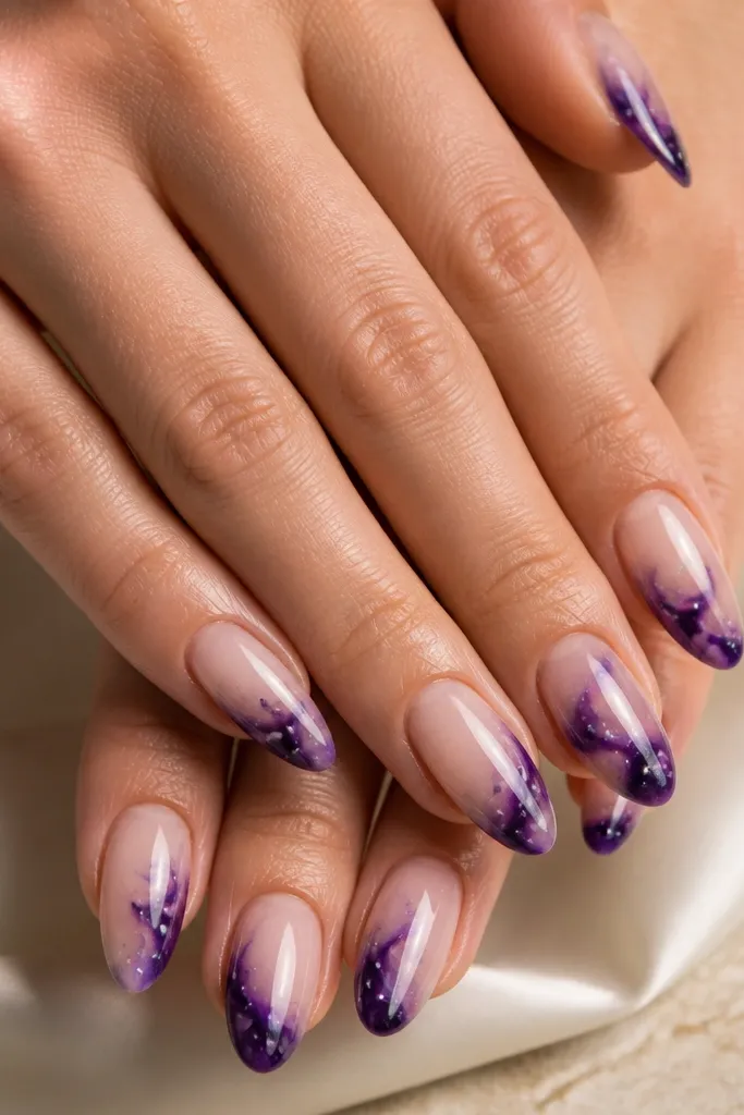 Almond nails with a nude base; swirls of dark purple near the tips and cuticles, with tiny white and silver specks like stars, finished glossy.